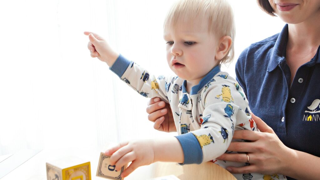 Pedagogisch medewerker helpt een baby bij het spelen aan tafel